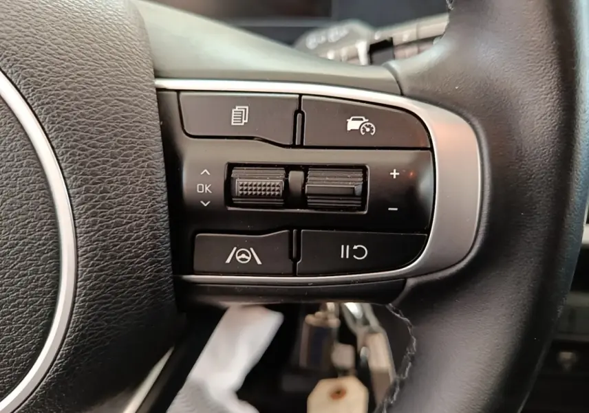 Gros plan sur les commandes multifonctions noires du volant cuir du KIA SPORTAGE beige 2022, côté gauche.