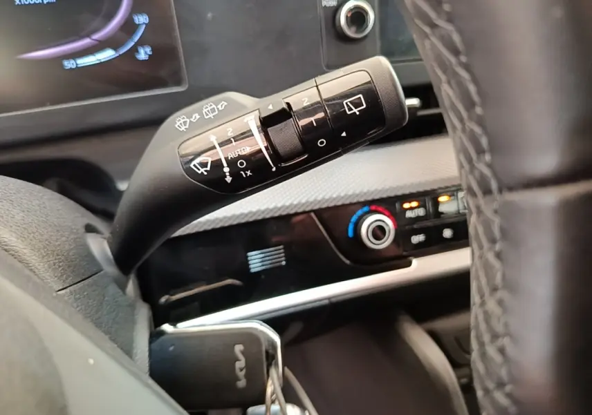 Gros plan sur la commande d’essuie-glace à gauche du volant du Kia Sportage beige, avec tableau de bord et climatisation visibles.
