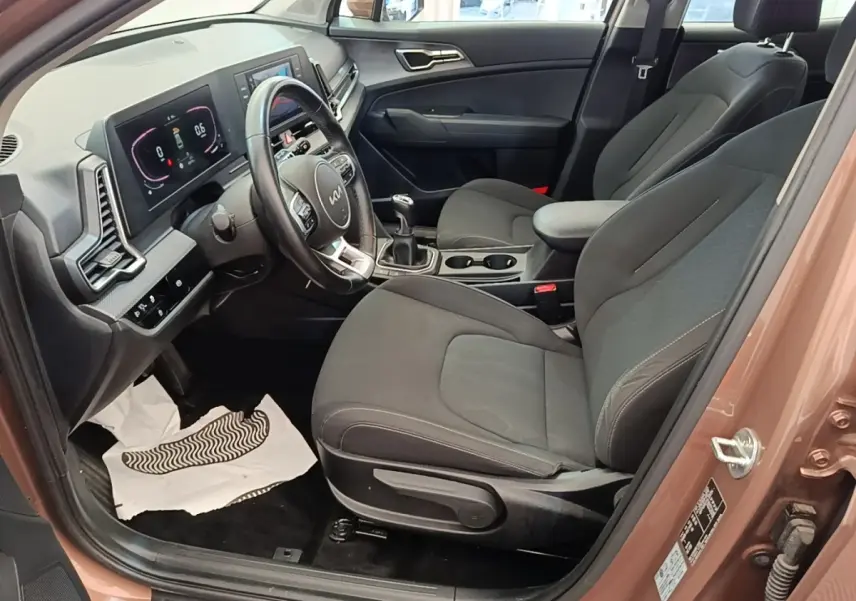 Vue intérieure côté conducteur du Kia Sportage beige 2022, avec sièges noirs, volant cuir multifonctions et tableau de bord digital.