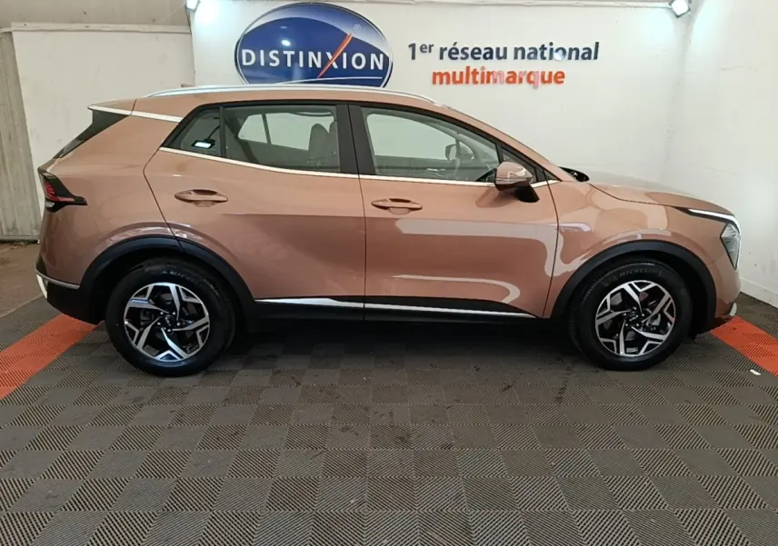 Profil droit d'un KIA SPORTAGE beige 2022 avec jantes alliage et rétroviseurs électriques dans un showroom.