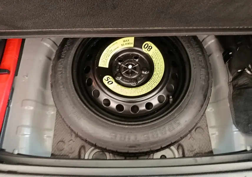 Roue de secours compacte noire visible dans le coffre d’un KIA SPORTAGE beige, vue en plongée.