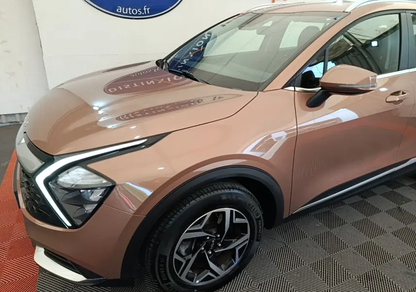 Vue 3/4 avant droit d’un Kia Sportage beige 2022 avec phares LED en forme de boomerang et jantes alliage noires.