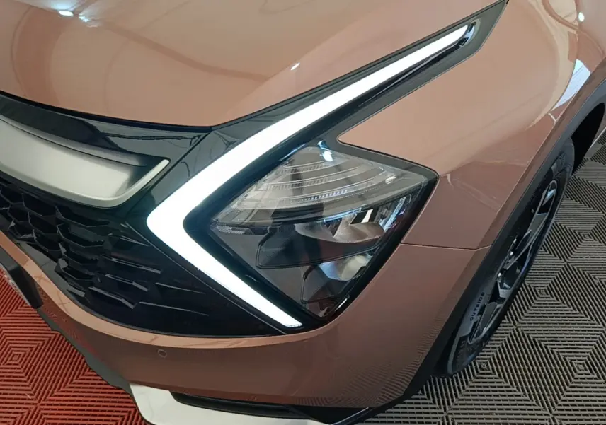 Gros plan sur l'avant droit beige du KIA Sportage 2022, mettant en valeur le phare LED en forme de boomerang.