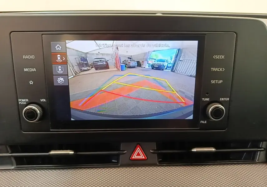 Écran tactile affichant la caméra de recul avec lignes de guidage colorées dans un Kia Sportage beige.
