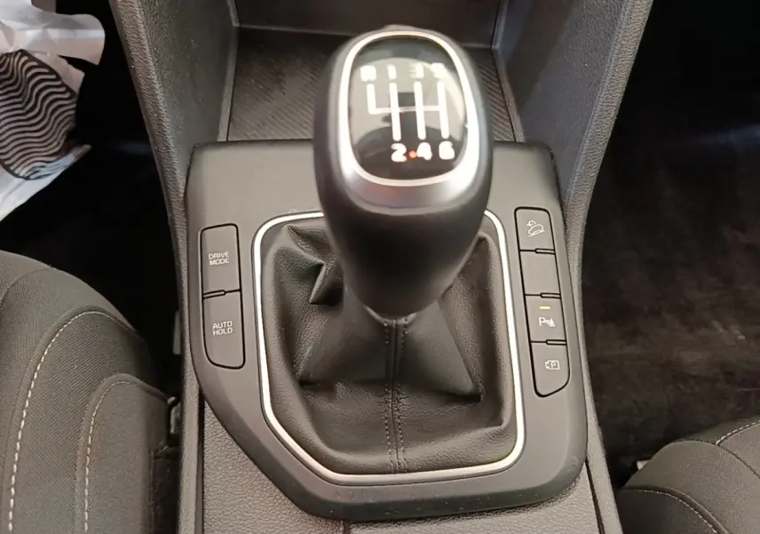 Gros plan sur le levier de vitesses manuel noir du Kia Sportage beige, entouré de boutons de contrôle sur la console centrale.