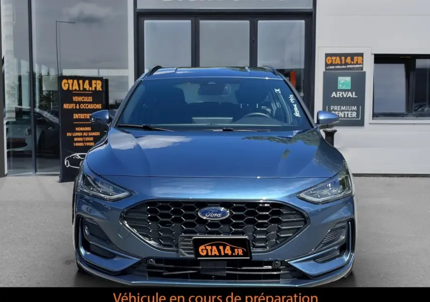 Vue frontale d'une Ford Focus SW bleue 2025 avec calandre hexagonale et phares effilés, stationnée devant un bâtiment.