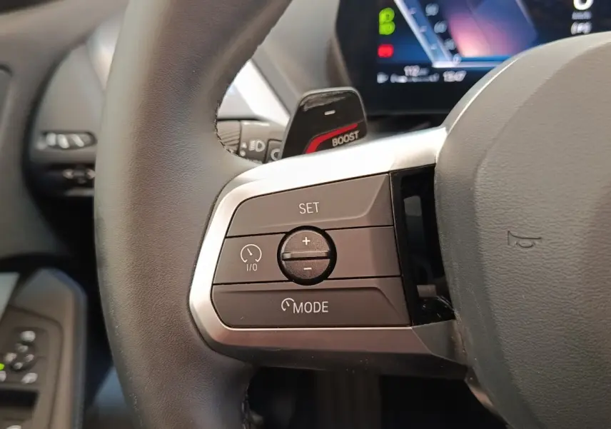 Gros plan sur les commandes à gauche du volant cuir noir de la BMW Série 1 120 DKG7 M Sport 2025.