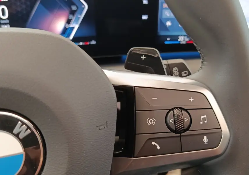 Gros plan sur les commandes multifonctions à droite du volant cuir gris d’une BMW Série 1 120 DKG7 M Sport 2025.