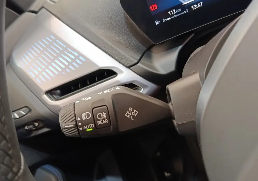 Gros plan sur la commande des feux et clignotants dans l’habitacle d’une BMW Série 1 gris clair, affichage numérique partiel visible.