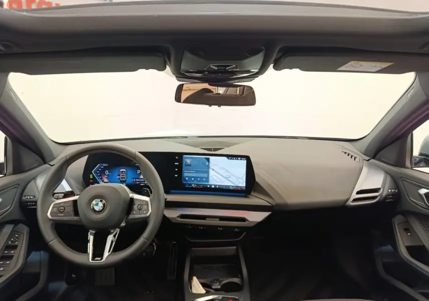 Vue intérieure avant de la BMW Série 1 120 DKG7 M Sport 2025, tableau de bord numérique et écran tactile central.
