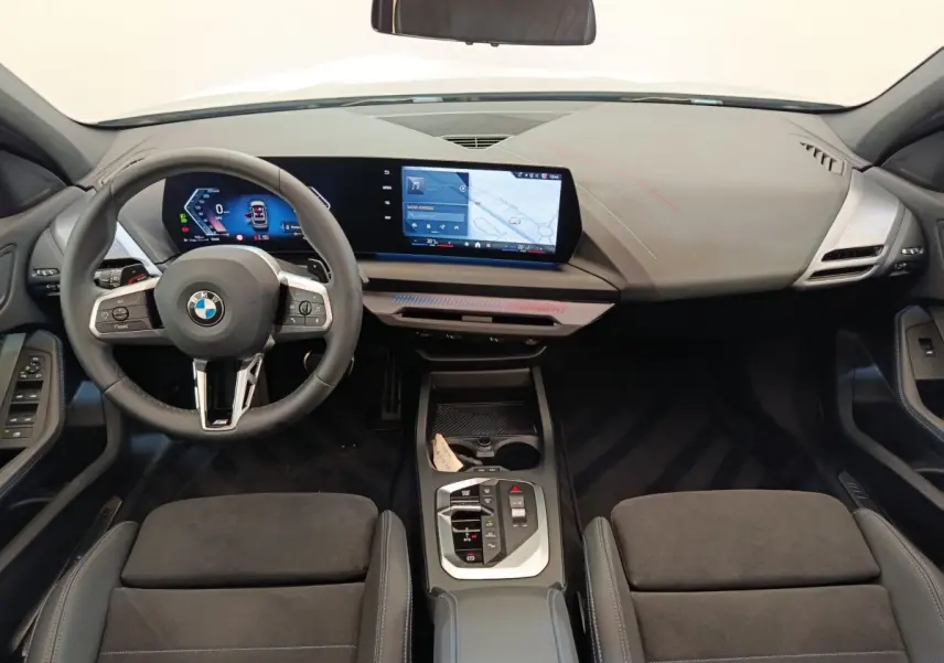 Vue intérieure avant de la BMW Série 1 120 DKG7 M Sport 2025, tableau de bord noir avec écran tactile large et volant cuir.