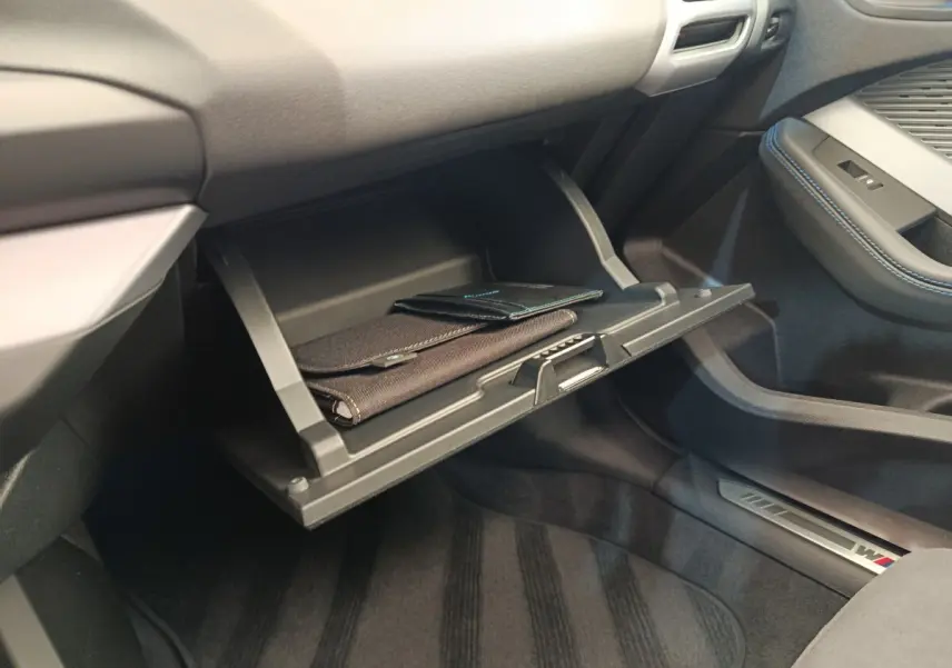 Intérieur BMW Série 1 120 DKG7 M Sport 2025, vue sur boîte à gants ouverte avec documents, sellerie noire et surpiqûres bleues.