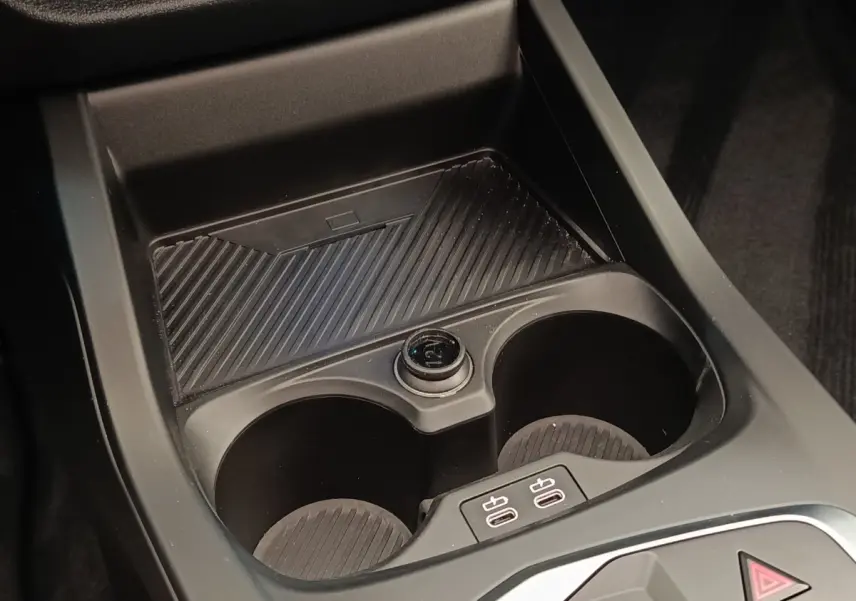 Gros plan sur la console centrale noire de la BMW Série 1 120 DKG7 M Sport avec porte-gobelets et prises USB.