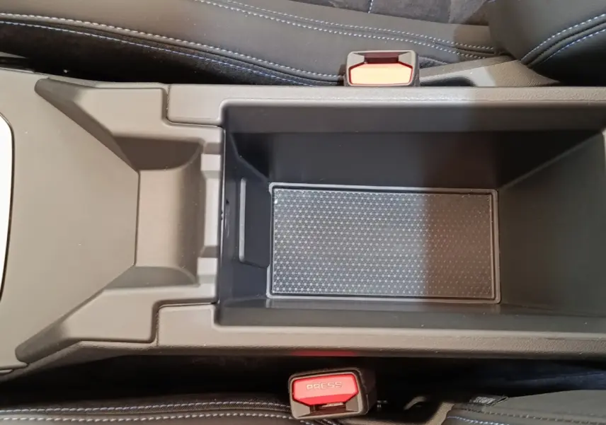 Vue plongeante sur le rangement central intérieur de la BMW Série 1 120 DKG7 M Sport 2025, avec sièges noirs et ceintures rouges.