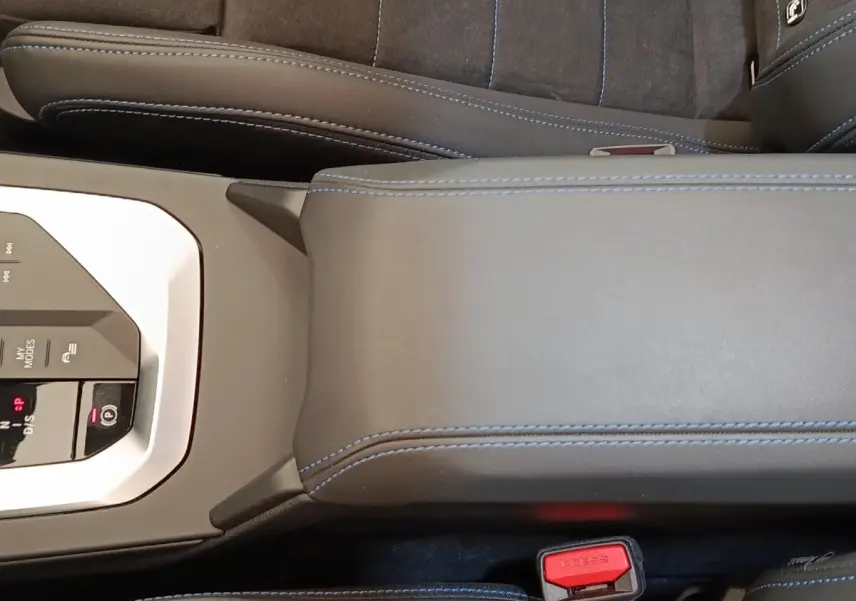 Vue rapprochée de la console centrale et accoudoir en cuir noir avec surpiqûres bleues de la BMW Série 1 120 DKG7 M Sport.
