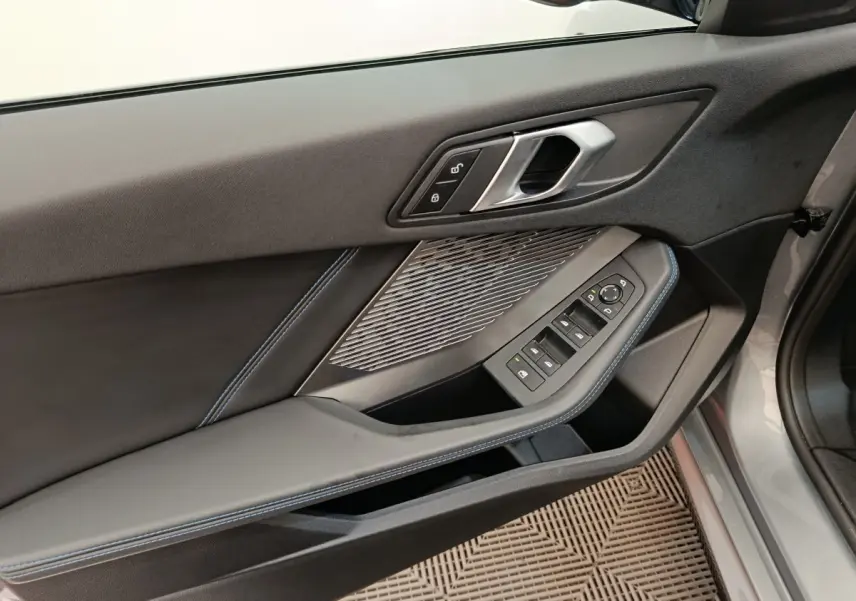 Vue rapprochée de la porte avant gauche grise d’une BMW Série 1 120 DKG7 M Sport avec commandes de vitres et serrure.