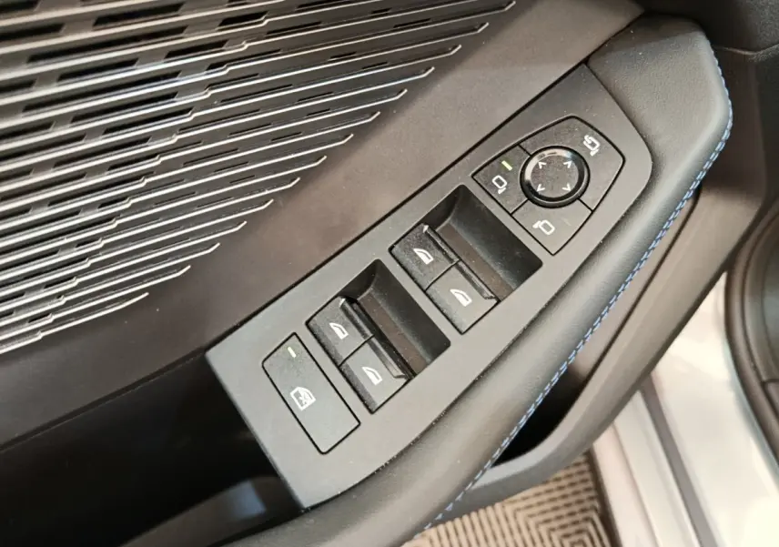Gros plan sur les commandes des vitres et rétroviseurs côté conducteur d’une BMW Série 1 gris clair, intérieur noir avec surpiqûres bleues.