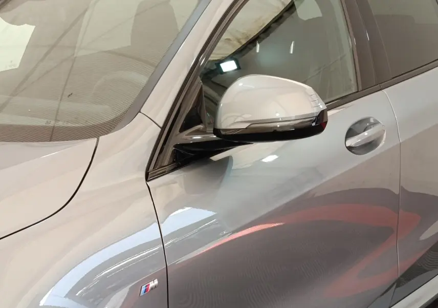 Gros plan sur le côté gauche gris clair de la BMW Série 1 120 DKG7 M Sport avec rétroviseur et logo M visibles.