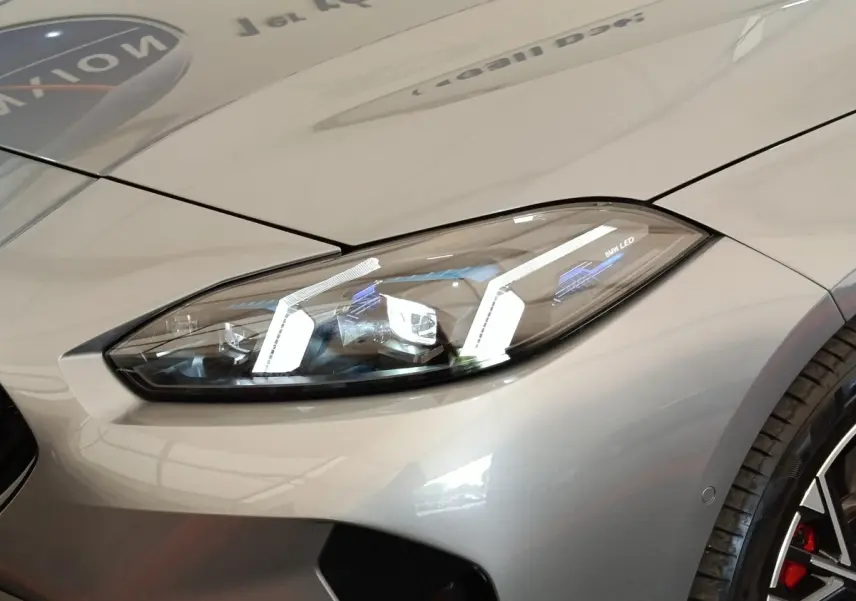 Gros plan sur le phare avant droit LED d’une BMW Série 1 gris clair avec jante sport et étrier rouge visible.