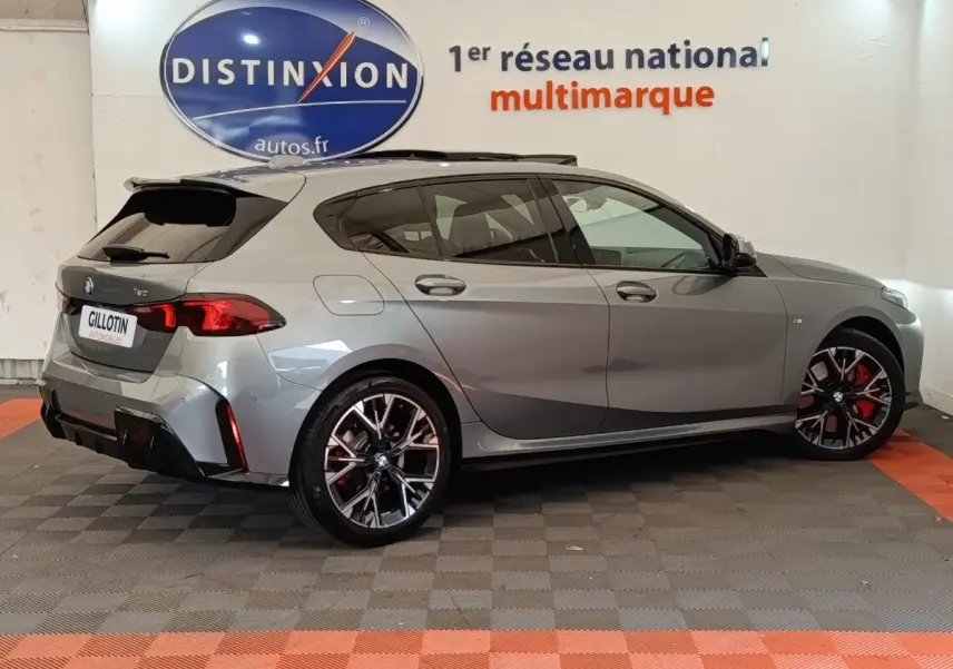 BMW Série 1 120 DKG7 M Sport gris clair vue de profil droit, avec jantes noires et étriers rouges visibles.
