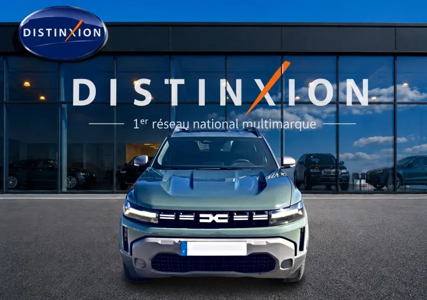 Vue frontale d'un Dacia Duster 1.2 hybrid-g 150 expression 4x4 en kaki lichen devant une vitrine Distinxion.