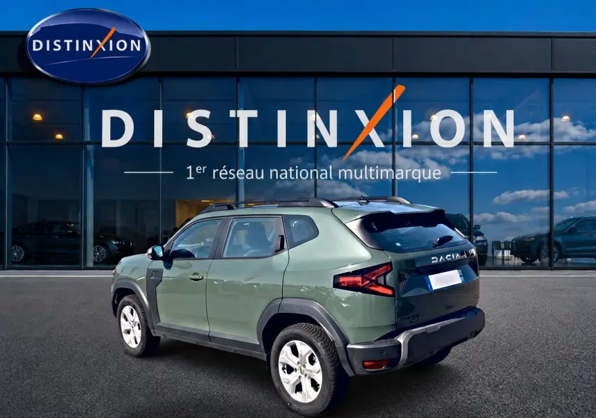 Dacia Duster 1.2 hybrid-g 150 expression 4x4 kaki lichen vu en 3/4 arrière droit devant un showroom Distinxion.