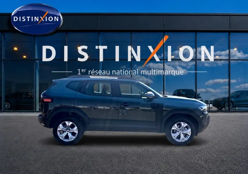 Profil côté gauche du Dacia Duster 2026 en kaki lichen, avec jantes alu et rétroviseurs chromés devant une vitrine Distinxion.