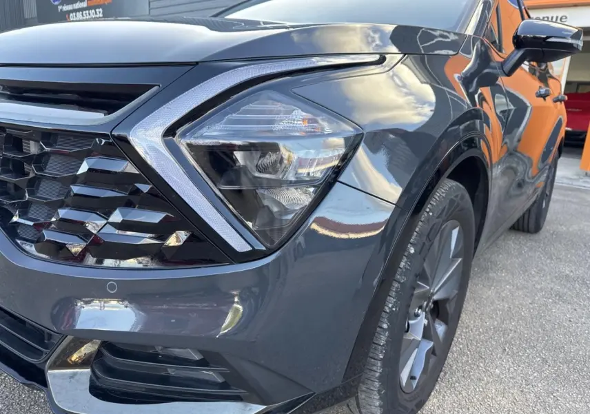 Gros plan sur l'avant droit du Kia Sportage gris Eclipse Métallisée, mettant en valeur le phare et la calandre distinctive.