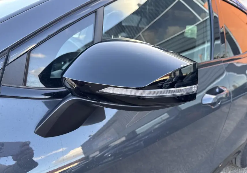Rétroviseur noir brillant avec clignotant intégré sur le côté gauche d’un KIA Sportage gris Eclipse Métallisée.
