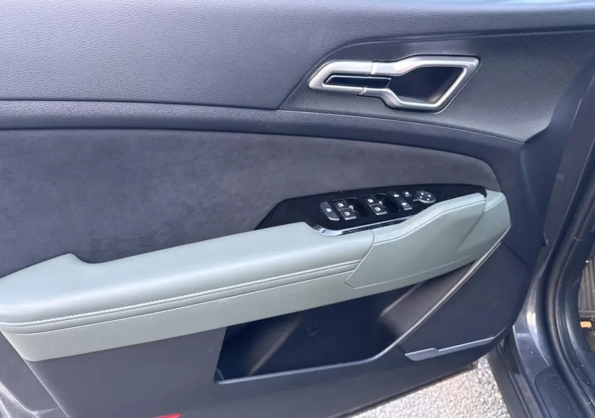 Vue rapprochée de la porte avant gauche du KIA SPORTAGE gris Eclipse Métallisée avec commandes de vitres et poignée intégrée.