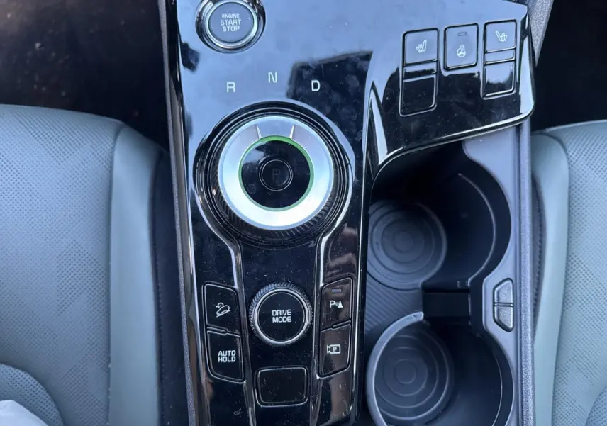 Vue plongeante sur la console centrale noire brillante du Kia Sportage gris, avec sélecteur rotatif et boutons chauffants.