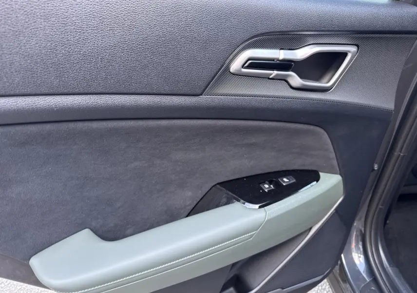Vue rapprochée de la porte avant gauche du KIA Sportage gris Eclipse avec accoudoir vert pin et commandes de vitres.