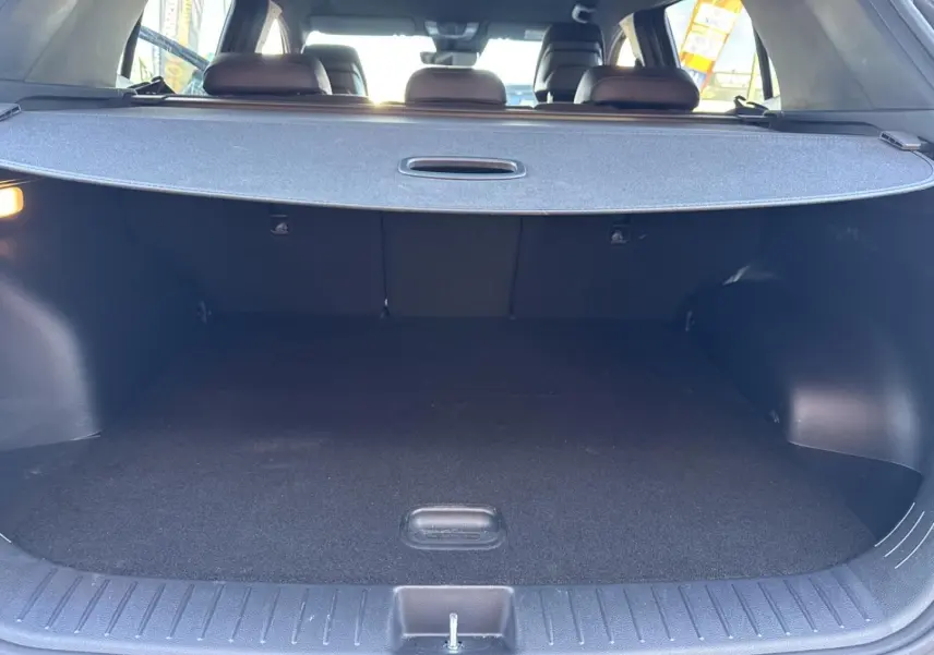 Coffre ouvert vu de l’arrière d’un KIA Sportage gris Eclipse avec cache-bagages déployé et banquette arrière visible.