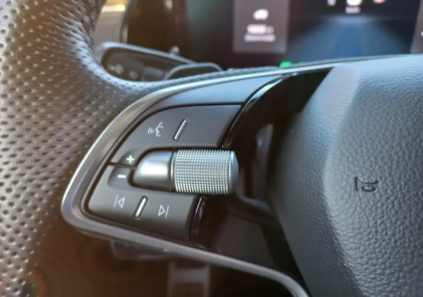 Gros plan sur les commandes gauche du volant perforé d’un Skoda Kodiaq Bleu RS 2024 avec molette métallique texturée.