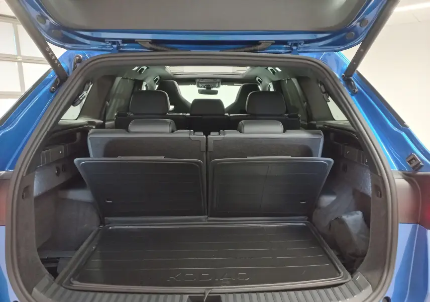 Vue arrière du coffre ouvert du Skoda Kodiaq Bleu RS 2024, montrant les sièges arrière et le tapis de coffre KODIAQ.