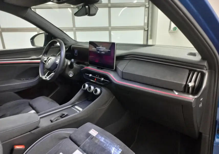 Intérieur côté conducteur du Skoda Kodiaq 2024 bleu RS, avec tableau de bord noir et bande rouge lumineuse.