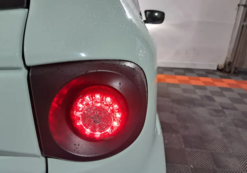 Gros plan sur le feu arrière droit rouge d'une Aixam Minauto E chic 2026 vert clair avec gouttes d'eau.