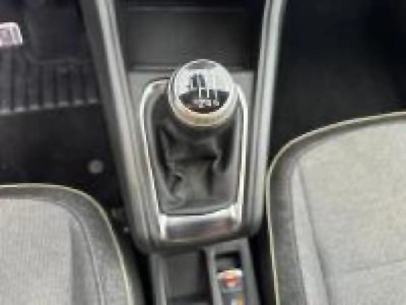 Vue plongeante sur le levier de vitesses manuel gris et noir entre les sièges tissu gris du Renault Captur rouge 2025.