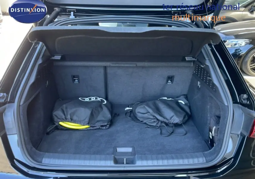 Coffre ouvert d’une Audi A3 Sportback noir mito metal, vue arrière montrant un espace de rangement avec deux sacs noirs.