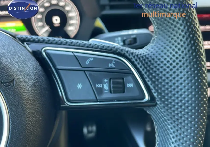 Gros plan sur le volant perforé de l'Audi A3 Sportback noir mito metal, avec commandes audio et téléphone intégrées.