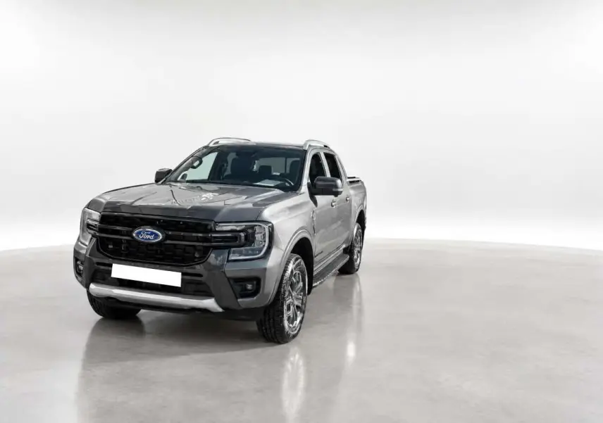 Ford Ranger 2.0 Wildtrak gris carbone en 3/4 avant droit, avec calandre noire et barres de toit visibles.
