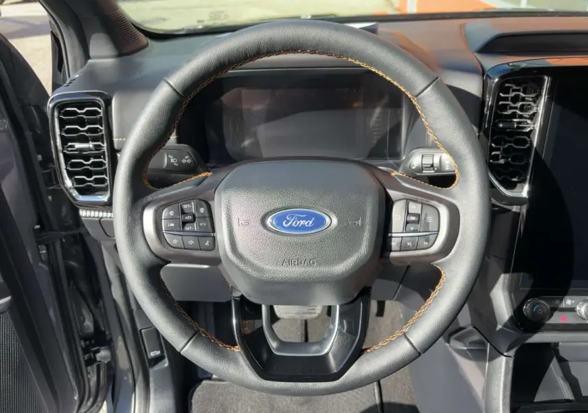 Vue rapprochée du volant cuir noir avec surpiqûres marron du Ford Ranger Wildtrak 2026, tableau de bord en arrière-plan.