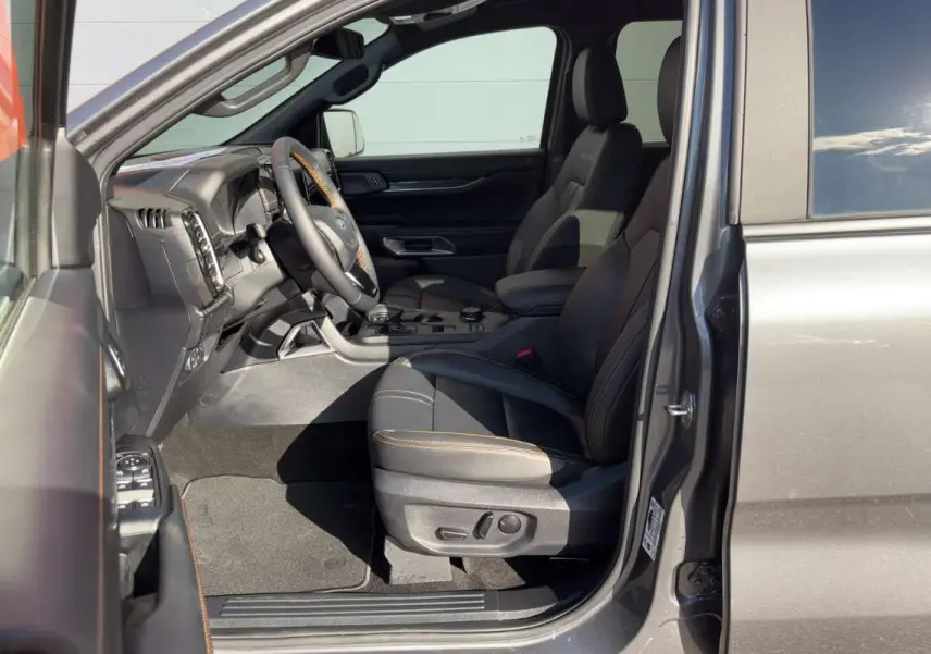 Vue intérieure côté conducteur du Ford Ranger gris carbone 2026, sièges en cuir avec surpiqûres orange et volant multifonctions.