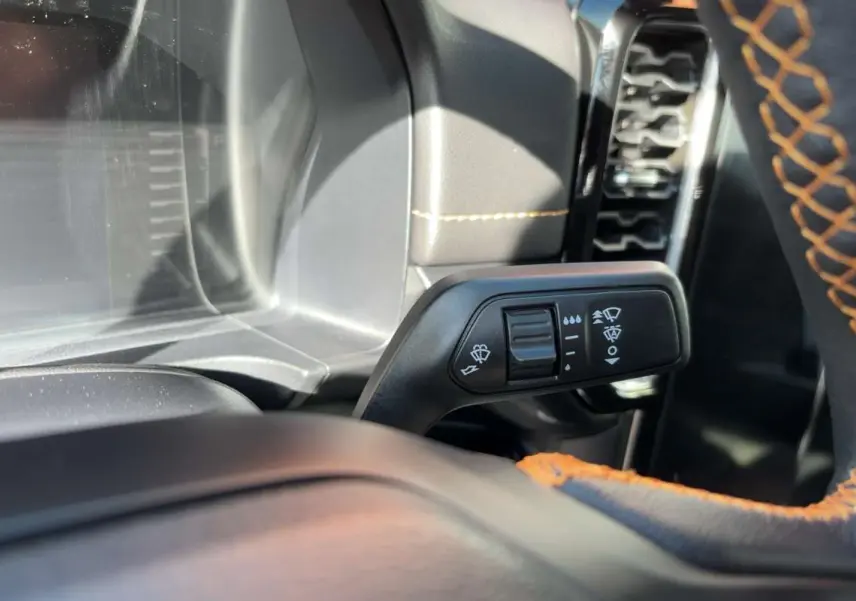 Gros plan sur la commande des essuie-glaces à gauche du volant cuir noir avec surpiqûres orange du Ford Ranger gris carbone.
