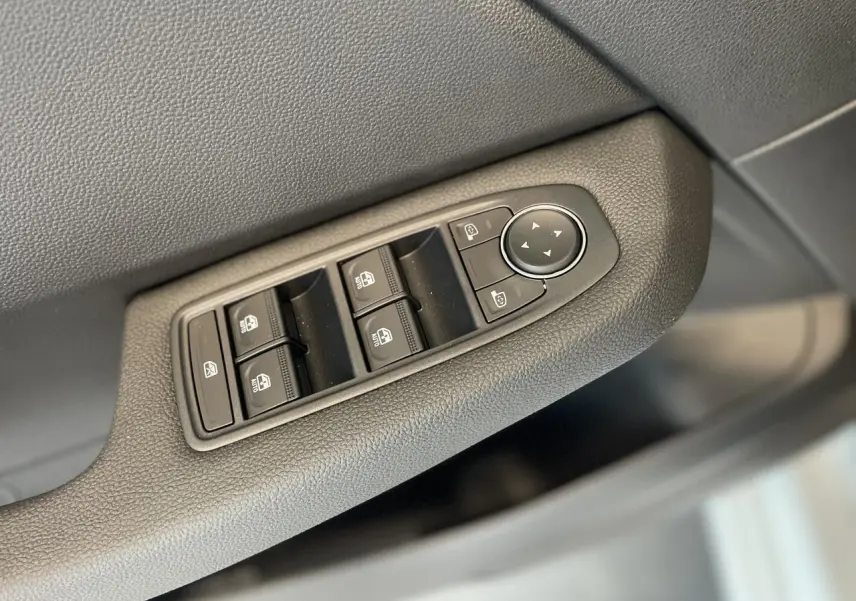 Gros plan sur les commandes des vitres électriques et rétroviseurs côté conducteur d'une Renault Clio blanche 2025.