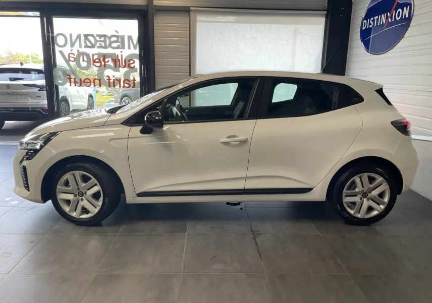 Profil côté gauche d'une Renault Clio blanche 2025 avec jantes alliage et poignées couleur carrosserie dans un showroom.