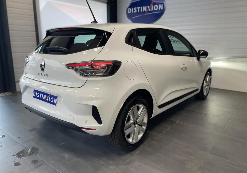 Vue 3/4 arrière droite d'une Renault Clio blanche Glacier avec feux arrière LED et jantes alliage en intérieur showroom.