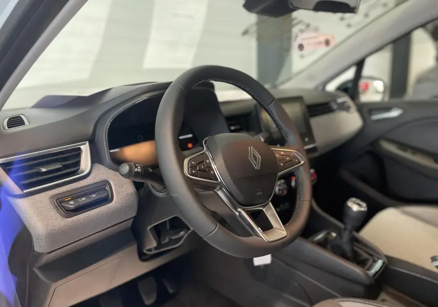 Intérieur Renault Clio 2025 vu côté conducteur, volant multifonction noir et tableau de bord avec inserts gris mozaic.