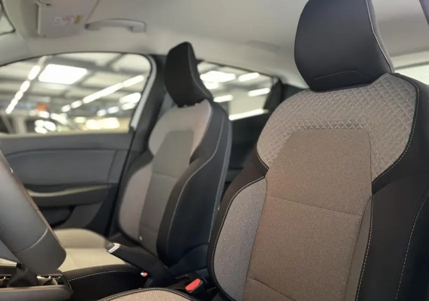 Vue intérieure rapprochée des sièges avant gris et noirs de la Renault Clio 2025 avec coutures blanches apparentes.