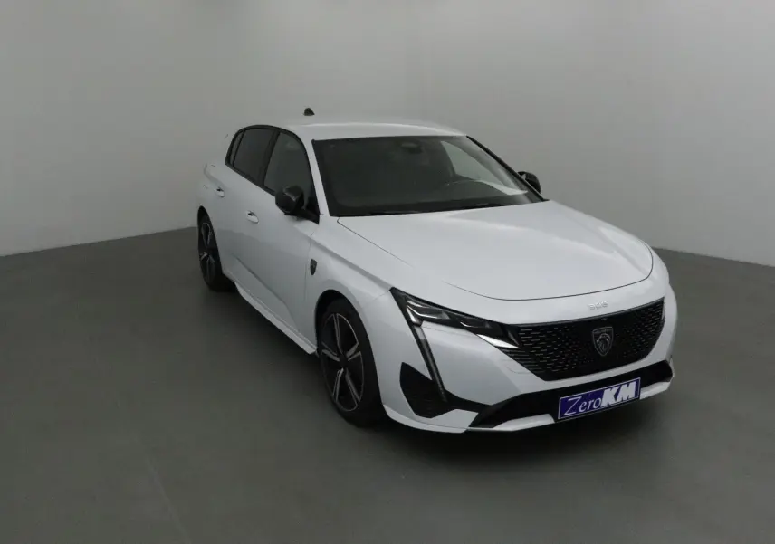 Peugeot 308 blanc Okenite vue 3/4 avant droit, avec calandre noire et feux LED en forme de griffes.